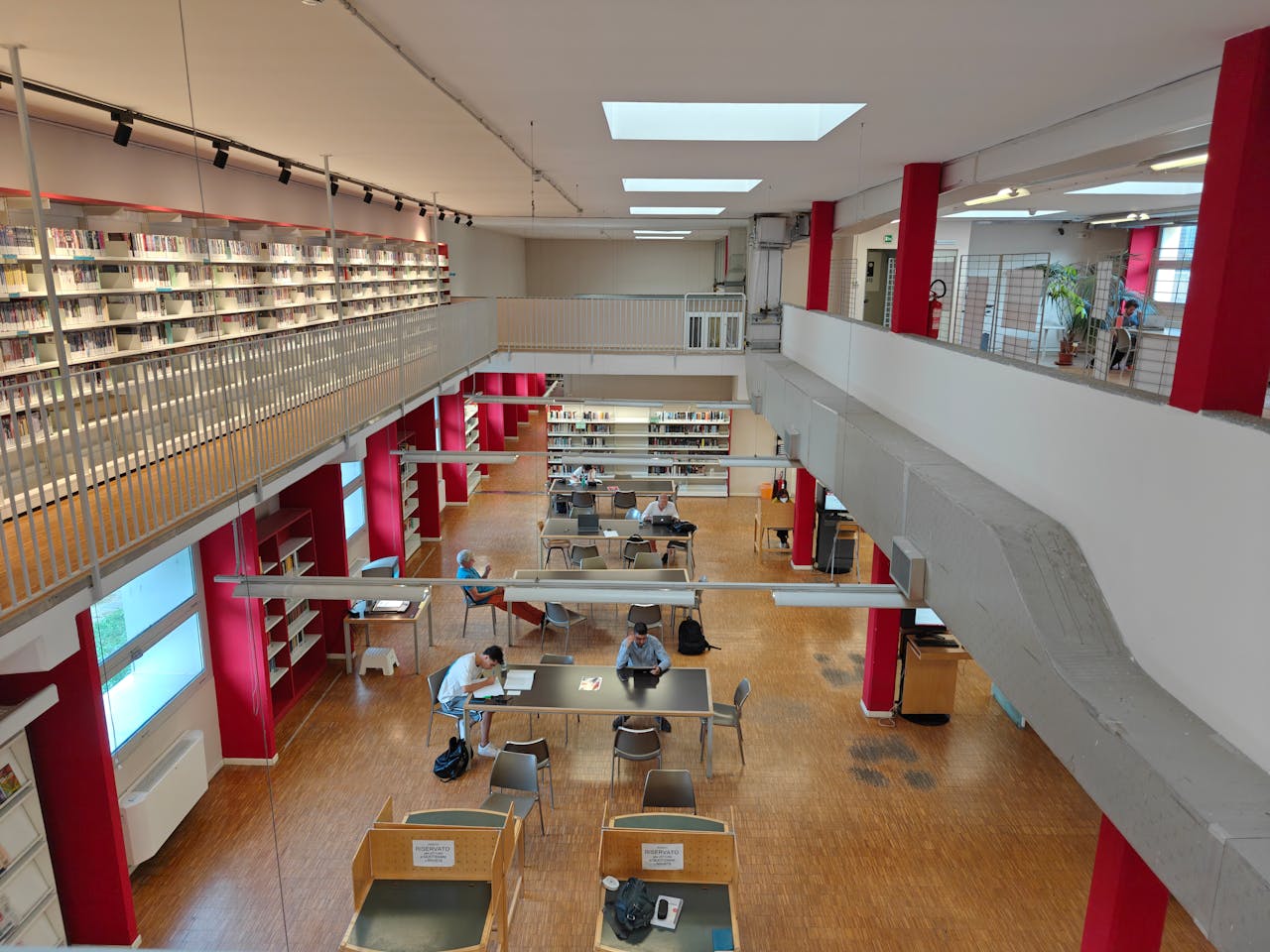 Bright library interior with students studying at tables, viewed from above.