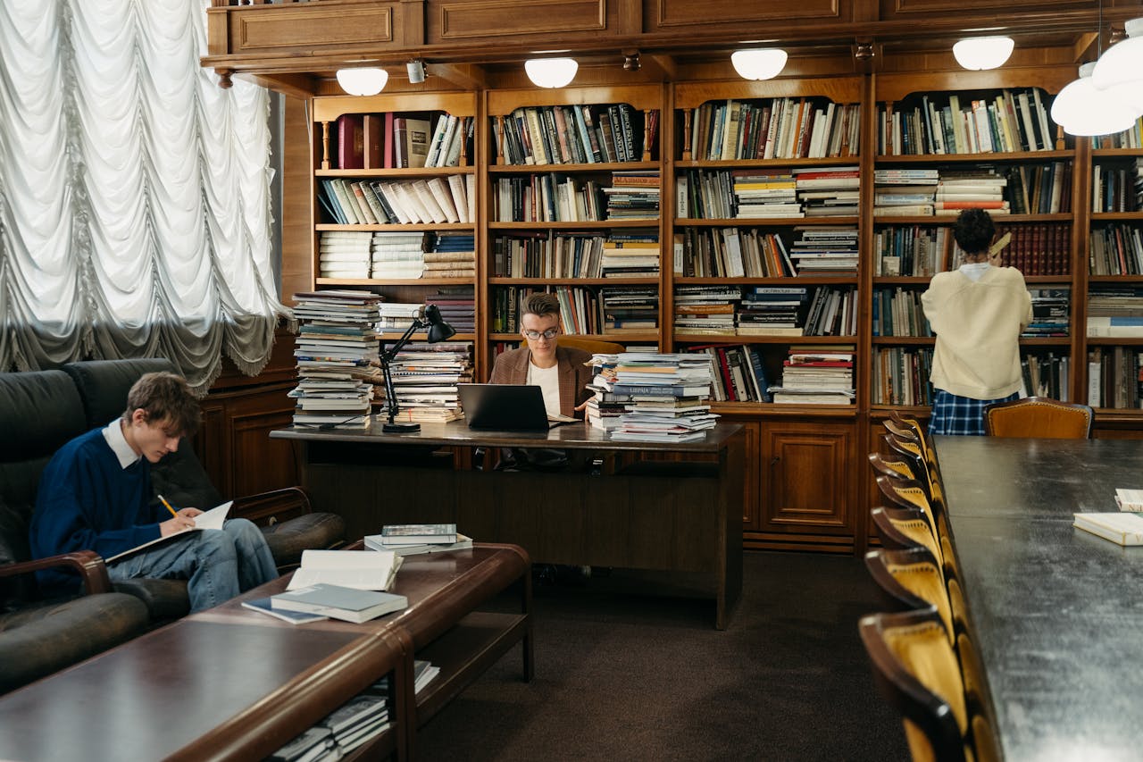 Students studying in a spacious library, surrounded by wooden shelves filled with books.